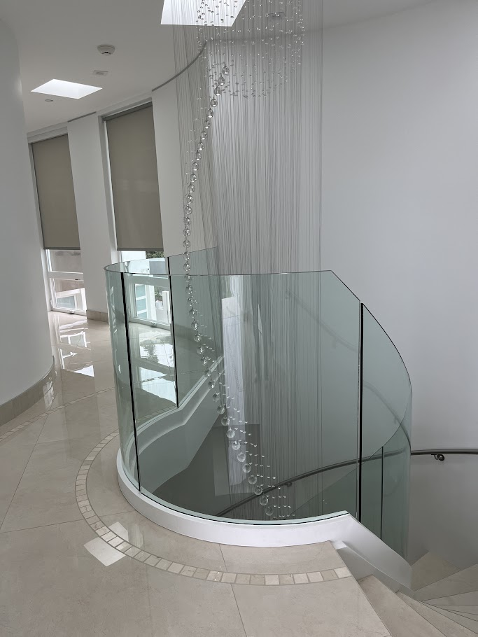 Spiral staircase with glass railing and chandelier.